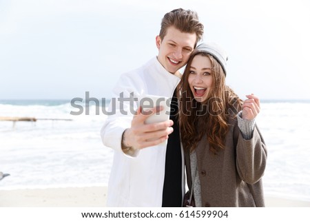 Happy young couple taking selfie with cell phone on the beach in autumn