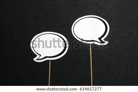 2 blank speech bubbles on a dark black background. Chat bubble cut from paper with wooden stick. Fun discussion, protesting and commenting concept with plenty of free copy space for your own text.