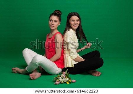 Two brunette girlfriends posing on green background in studio