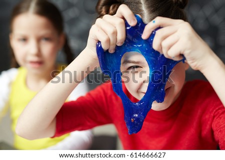 Happy kid looking through hole in blue slime Royalty-Free Stock Photo #614666627