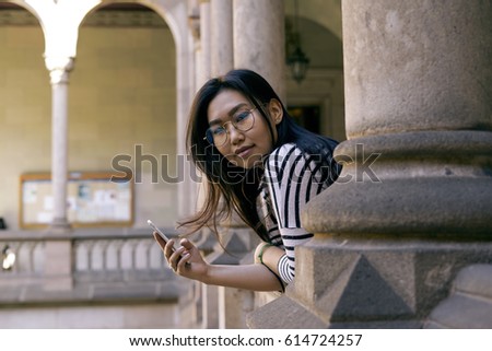 Photo of the beautiful model look asian female looking at the camera and holding a smartphone in the hand. Travel blogger wearing casual clothes it reading email on the screen of the a cell phone.