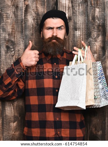 Bearded man, long beard. Brutal caucasian serious hipster with moustache holding shopping packages in red black checkered shirt on brown wooden vintage studio background