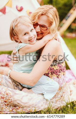 Woman kisses little girl's cheek tender sitting before white tent