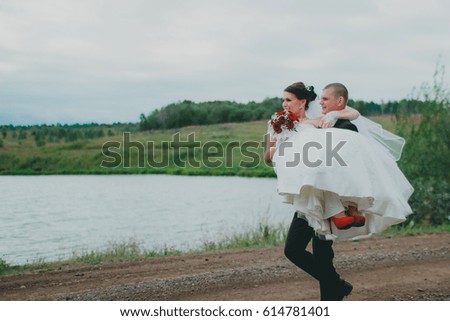 the groom carries the bride on background of lake