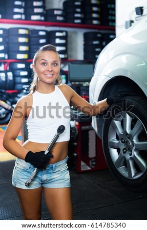 Attractive young mechanic woman working on car wheel in service point
