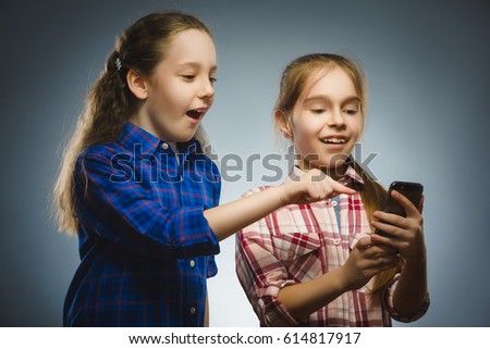 Two little happy girls using mobile or cell phone isolated grey background