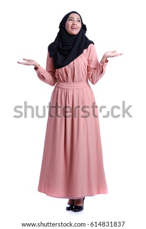 Studio photography of young happy beautiful Asian muslim woman smiling and showing something. Royalty-Free Stock Photo #614831837