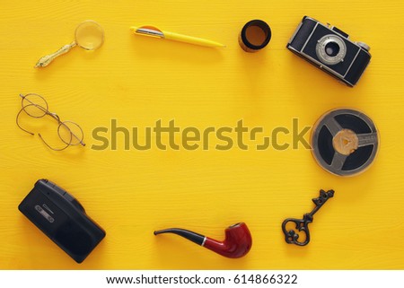 top view image of old camera, film and tape recorder over wooden yellow background. journalism or detective concept