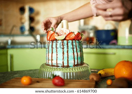 Cake of green color with chocolate, fruits and flowers, the girl decorates it with her hands