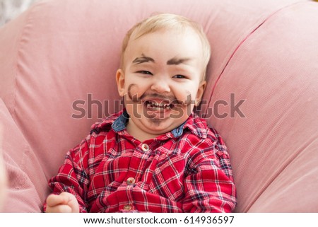Portrait of a small baby, a boy with a dirty face painted with a beard and mustache. He's laughing