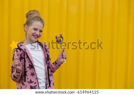 Portrait of a beautiful girl with red lips on a yellow background outdoors in summer. Young girl with lollipops against the yellow wall background