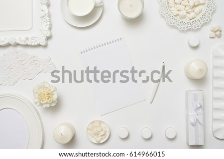 Top view shot of a workspace desk with empty notebook and pen surrounded with accessories. White candles and flowers