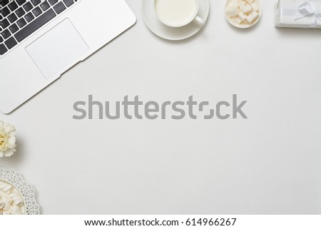 Cropped overhead shot of an office desktop with laptop computer, cup of milk and flower arranged on a white background. Flat lay picture 