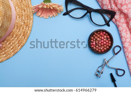 Top view of clothes with cosmetics on blue background, flat lay picture. Cosmetic set of various items and bronzed pearls