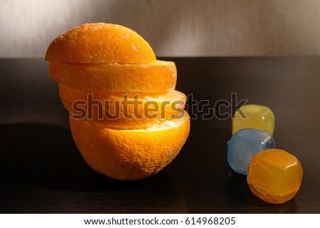 frozen fresh orange on black table sliced and stacked on one another near in corner multi colored three cubes of plastic ice for drink lighting by spot