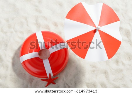 Red and white umbrella and swimming ring at the beach: top view