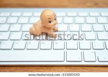 Little toy doll baby on the white keyboard lying on the table, blurry