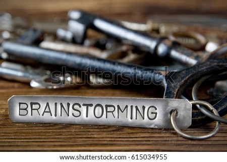 Photo of key bunch on wooden board and tag with letters imprinted on clean metal surface; concept of BRAINSTORMING