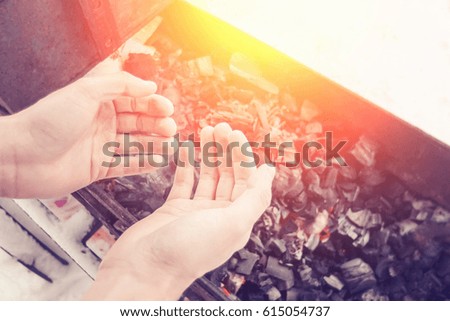Man warms his hands over coals in the grill in winter