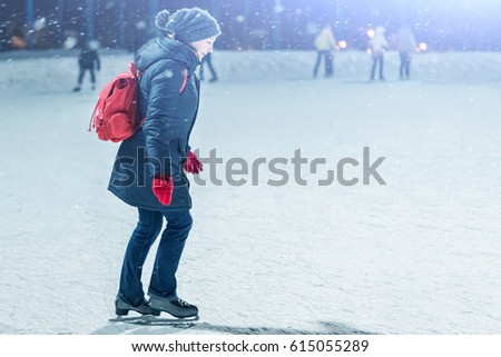 Beautiful woman with a red backpack on a skating rink in the evening