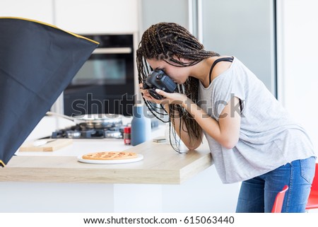 Side view of young woman with braids in grey T-shirt taking picture of pizza on wooden table surface in studio