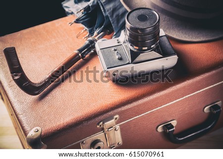 Adventure concept. Old film camera with vintage hat and umbrella on old brown suitcase. Vintage toned image