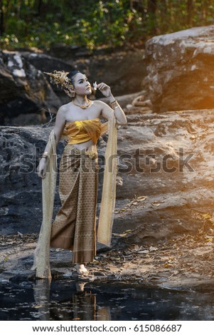 Beautiful young woman dressed in retro Thai dress near waterfall in the forest.