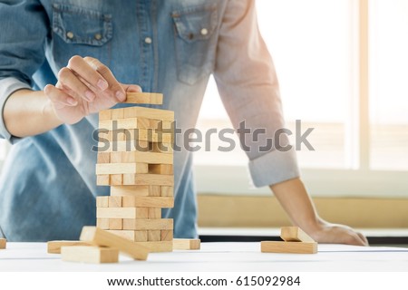 Hand of engineer playing a blocks wood tower game (jenga) on blueprint or architectural project Royalty-Free Stock Photo #615092984