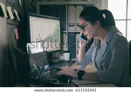 seriously young woman sitting at her desk answering a phone call and holding pen using laptop keyboard. office lady working at night overtime.