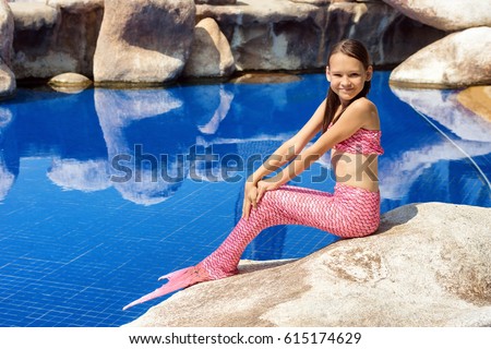 Mermaid girl with pink tail on rock at poolside. Fun, fashion concept. Text space