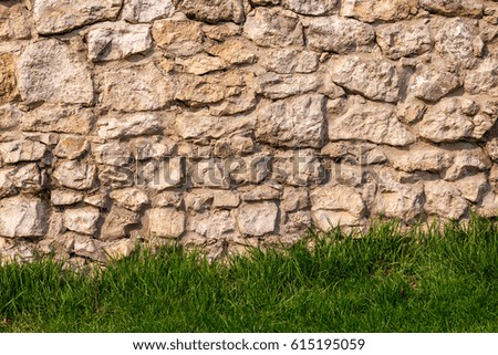 Rough old sandstone castle wall background and texture with green grass lawn at the bottom