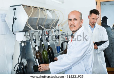 Glad mature man employee in white coat testing bottling equipment on a modern facility 