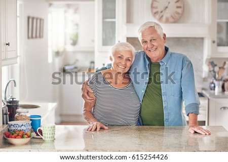 Portrait of a content senior man with his arm around his wife's shoulder standing together in their  kitchen at home Royalty-Free Stock Photo #615254426