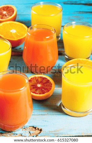 Concept of summer refreshing drink and fruits, bright colors. Glasses with juice from classic and Sicilian oranges, halves of oranges. On an old rustic blue wooden table. Copy space