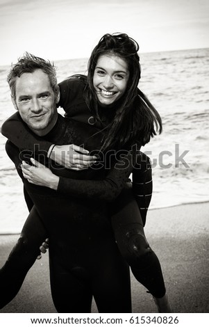 At the beach, looking at camera, a couple wearing wetsuit having fun. Black and white picture