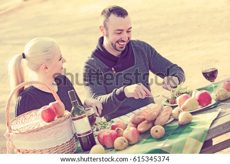 Portrait of young adults drinking wine at table in nature and smiling