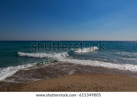 The surf of the blue turquoise sea with white perpendicular waves on the sandy beach against a bright clear sky. Kassandra, Â Chalkidiki, Greece