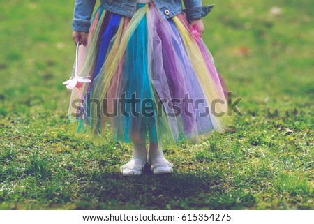 Little girl in colorful tutu skirt standing on green grass while holding magic wand