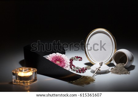 white urn with blank mourning frame, flower, tape, candle and rosary for sympathy card on dark background