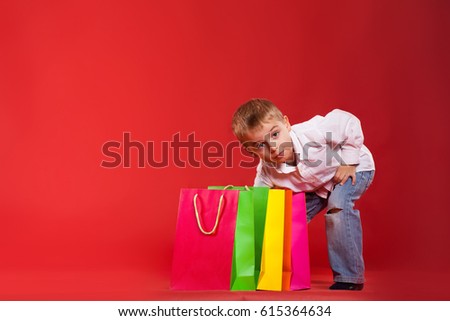 Little boy peers into his packages with gifts on a red background