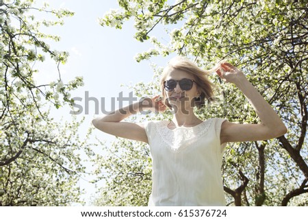 Dancing young woman in the spring blooming garden in the white dress and sunglasses