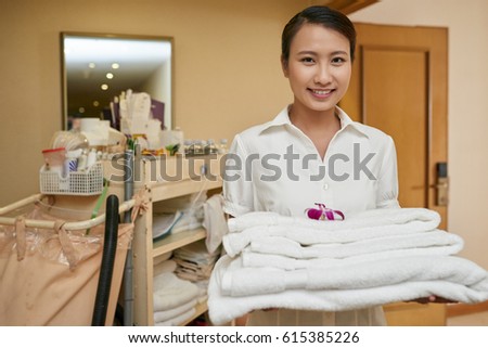Cheerful Vietnamese chambermaid with stack of white towels
