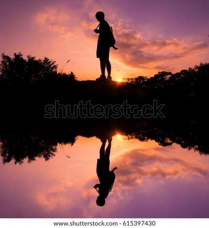 A man standing at the sunset silhouette with water reflection