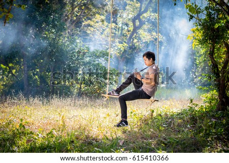 Young man is playing an old camera while sitting on a swing in the forest.