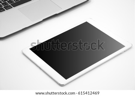 White tablet computer with blank screen and laptop on white background