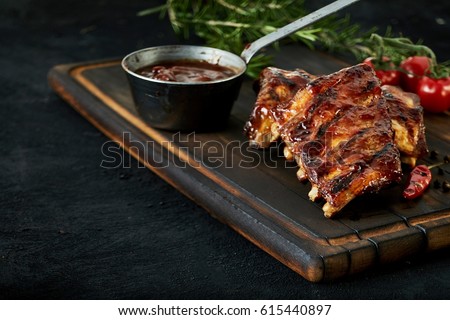 Spicy rack of spare ribs with marinade in a small saucepan and a red hot chili pepper served on an old wood chopping board in a restaurant , close up view with copy space Royalty-Free Stock Photo #615440897