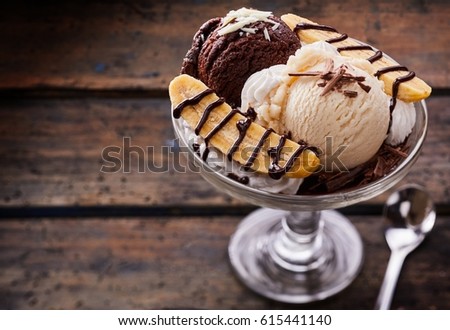 High Angle Close Up View of Banana Split with Scoops of Vanilla and Chocolate Ice Cream, Sliced Bananas, and Chocolate Sauce Served in Glass Dish on Rustic Wooden Table with Silver Spoon Royalty-Free Stock Photo #615441140