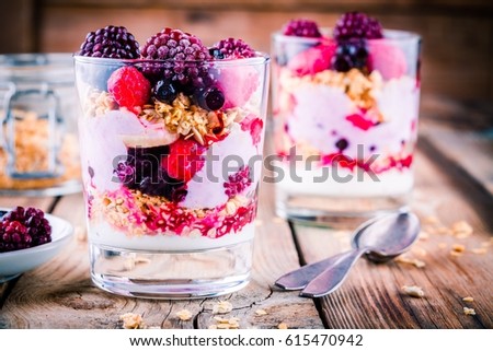 Healthy breakfast: yogurt parfait with granola and raspberry, blueberry, banana and frozen blackberry on wooden table