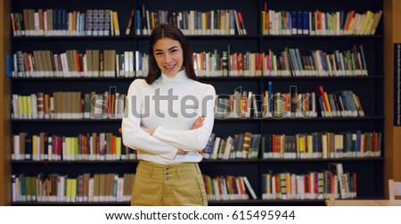 Portrait of a beautiful young woman smiling happy in a library holding books after doing a search and after studying. Concept: educational, portrait, library, and studious.