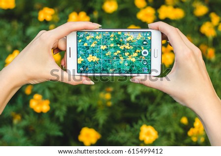 girl taking mobile photo with mobile phone on the background of green grass with flowers during an exercise break